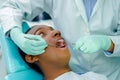 Young hispanic man lying in chair receiving dental treatment with mouth open, dentist hands wearing gloves holding tools Royalty Free Stock Photo