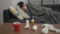 Young hispanic man lying on the sofa sick with tissues and pills on the table at home