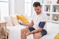 Young hispanic man measuring pulse using tensiometer at bedroom