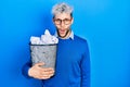 Young hispanic man with modern dyed hair holding paper bin full of crumpled papers scared and amazed with open mouth for surprise, Royalty Free Stock Photo