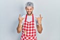 Young hispanic man with modern dyed hair wearing apron shouting with crazy expression doing rock symbol with hands up