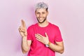 Young hispanic man with modern dyed hair wearing casual pink t shirt smiling swearing with hand on chest and fingers up, making a Royalty Free Stock Photo