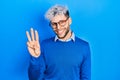 Young hispanic man with modern dyed hair wearing sweater and glasses showing and pointing up with fingers number three while Royalty Free Stock Photo