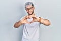 Young hispanic man with modern dyed hair wearing white t shirt and glasses smiling in love doing heart symbol shape with hands Royalty Free Stock Photo