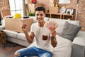 Young hispanic man moving to a new home holding shekels smiling happy pointing with hand and finger to the side Royalty Free Stock Photo