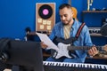 Young hispanic man musician playing electrical guitar reading music sheet at music studio Royalty Free Stock Photo