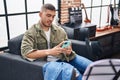 Young hispanic man musician using smartphone at music studio