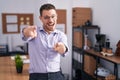 Young hispanic man at the office pointing to you and the camera with fingers, smiling positive and cheerful Royalty Free Stock Photo