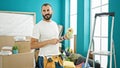 Young hispanic man painter holding paint roller thinking at new home Royalty Free Stock Photo