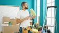 Young hispanic man painter holding paint roller thinking at new home Royalty Free Stock Photo