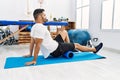 Young hispanic man patient smiling confident having leg rehab session using foam roller at clinic