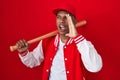 Young hispanic man playing baseball holding bat shouting and screaming loud to side with hand on mouth Royalty Free Stock Photo