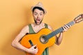 Young hispanic man playing classical guitar afraid and shocked with surprise and amazed expression, fear and excited face Royalty Free Stock Photo