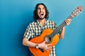 Young hispanic man playing classical guitar angry and mad screaming frustrated and furious, shouting with anger looking up Royalty Free Stock Photo