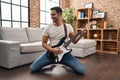 Young hispanic man playing electrical guitar with knees on floor at home Royalty Free Stock Photo