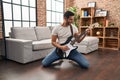 Young hispanic man playing electrical guitar with knees on floor at home