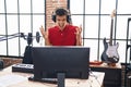 Young hispanic man playing piano keyboard at music studio crazy and mad shouting and yelling with aggressive expression and arms Royalty Free Stock Photo