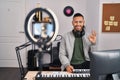 Young hispanic man playing piano at music studio recording himself doing ok sign with fingers, smiling friendly gesturing Royalty Free Stock Photo