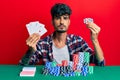 Young hispanic man playing poker holding cards and casino chips relaxed with serious expression on face Royalty Free Stock Photo