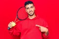 Young hispanic man playing tennis holding racket and ball smiling happy pointing with hand and finger Royalty Free Stock Photo