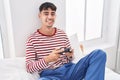 Young hispanic man playing video game sitting on bed at bedroom Royalty Free Stock Photo