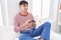 Young hispanic man playing video game sitting on bed at bedroom Royalty Free Stock Photo