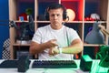 Young hispanic man playing video games in hurry pointing to watch time, impatience, upset and angry for deadline delay Royalty Free Stock Photo