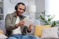 A young Hispanic man plays online games on a tablet at home. Sitting smiling on the couch wearing headphones Royalty Free Stock Photo