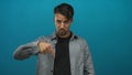 Young hispanic man pointing down against a blue background, emphasizing direction and focus in a casual setting, ideal for Royalty Free Stock Photo