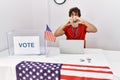 Young hispanic man at political election sitting by ballot smiling in love doing heart symbol shape with hands