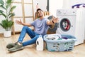 Young hispanic man putting dirty laundry into washing machine looking at the camera smiling with open arms for hug Royalty Free Stock Photo