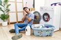 Young hispanic man putting dirty laundry into washing machine sleeping tired dreaming and posing with hands together while smiling Royalty Free Stock Photo