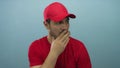 Young hispanic man in red cap and shirt with finger to lips for silence in light blue studio; silence Royalty Free Stock Photo
