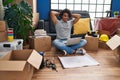 Young hispanic man relaxed with hands on head using laptop sitting on floor at new home Royalty Free Stock Photo