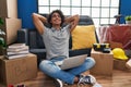 Young hispanic man relaxed with hands on head using laptop sitting on floor at new home Royalty Free Stock Photo