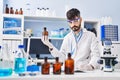 Young hispanic man scientist writing on notebook holding bottle at laboratory Royalty Free Stock Photo