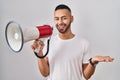 Young hispanic man shouting through megaphone celebrating achievement with happy smile and winner expression with raised hand