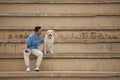 Young Hispanic man sitting on large cement stairs looking at his dog with pride and affection. Concept, dogs, pets, animals,