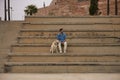 Young Hispanic man, sitting on large cement stairs next to his dog looking both in the same direction. Concept, dogs, pets,
