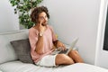 Young hispanic man sitting on the sofa at home using laptop pointing to the eye watching you gesture, suspicious expression Royalty Free Stock Photo