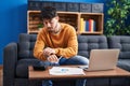 Young hispanic man sitting on sofa teleworking looking watch at home Royalty Free Stock Photo