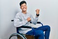 Young hispanic man sitting on wheelchair celebrating surprised and amazed for success with arms raised and eyes closed