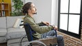 Young hispanic man sitting on wheelchair looking throw the window with sad expression at home Royalty Free Stock Photo