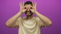 Young hispanic man smiles and forms playful binocular gesture with his hands in studio; playful curiosity Royalty Free Stock Photo