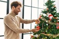 Young hispanic man smiling confident decorating christmas tree at home Royalty Free Stock Photo