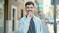 Young hispanic man smiling confident doing silent gesture at street