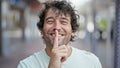 Young hispanic man smiling confident doing silent gesture at street