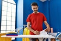 Young hispanic man smiling confident folding clothes at laundry room