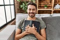 Young hispanic man smiling confident hugging bible at home Royalty Free Stock Photo