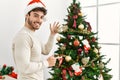 Young hispanic man smiling happy decorating christmas tree at home